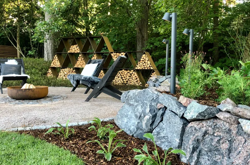 Rinnepihan pihasuunnitelma Espoossa – luonnonkivimuuri, tunnelmallinen pihavalaistus, istutusalueet ja nuotiopaikka viihtyisässä ulkoalueessa.